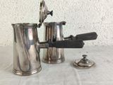 a silver coffee pot and a silver cup on a table