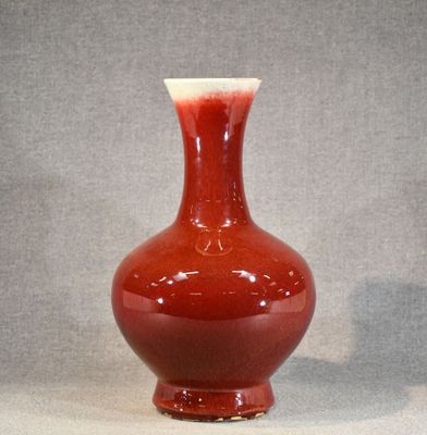 un vase rouge posé sur une table, sur fond gris