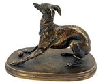 statue of a dog laying down on a base with a ball in it ' s mouth