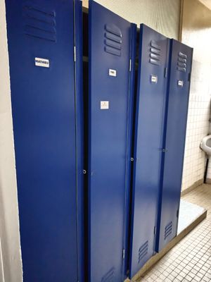 three blue lockers in a public bathroom with a urinal