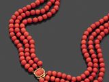 un gros plan sur un collier de perles rouges muni d'un fermoir doré