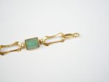 a close up of a gold bracelet with a green stone on it