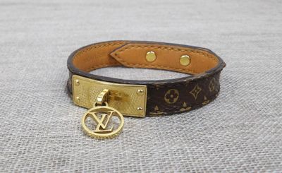a close up of a brown leather bracelet with a gold charm