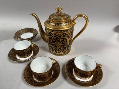 une théière en or et quatre tasses posées sur une table blanche