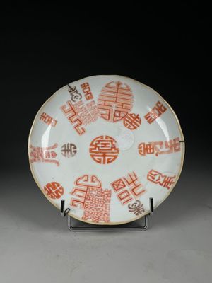 une assiette orange et blanche, ornée d'inscriptions en caractères asiatiques, posée sur un socle