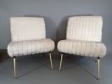 two white chairs with gold legs in a room with a gray wall