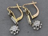 une paire de boucles d'oreilles en or et en argent, ornées de diamants, sur un fond gris