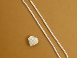 un collier de perles blanches et une broche en forme de cœur sur un fond marron
