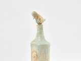 un oiseau perché sur une bouteille posée sur une surface blanche