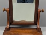un petit miroir en bois posé sur un support, avec une personne debout à l'arrière-plan