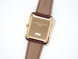 a gold watch with a brown leather strap on a white surface