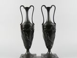 une paire de vases noirs posés sur des socles en marbre, sur fond blanc