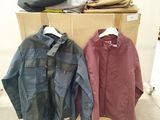 two jackets are hanging on a rack in front of a pile of clothes