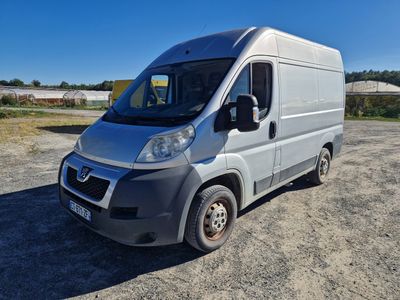 une camionnette argentée garée sur un parking en gravier, avec le ciel bleu en arrière-plan