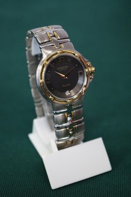 une montre en argent et en or exposée sur un socle blanc