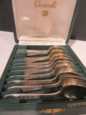 six cuillères en argent dans un étui vert, posées sur une table blanche