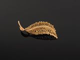 a gold leaf broochle on a black surface