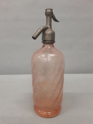 une vieille bouteille en verre rose munie d'un bec verseur en métal, posée sur une table