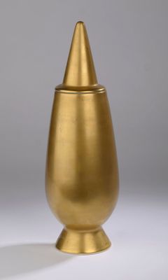 vase en métal doré, dont le sommet est de forme conique, posé sur un fond blanc
