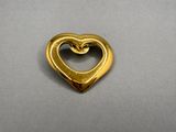 une image représentant un pendentif doré en forme de cœur posé sur une surface grise