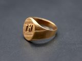 a close up of a gold signet ring with the letter t on it