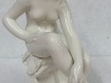 une statue blanche représentant une femme assise sur un rocher