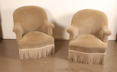 pair of beige upholstered chairs with fringes on the legs