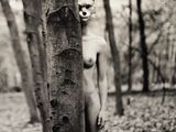 black and white photograph of a naked woman standing next to a tree in the woods