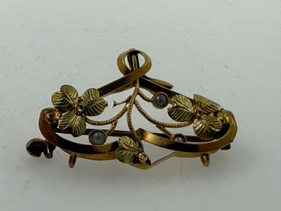 a gold brooch with leaves on it on a white surface