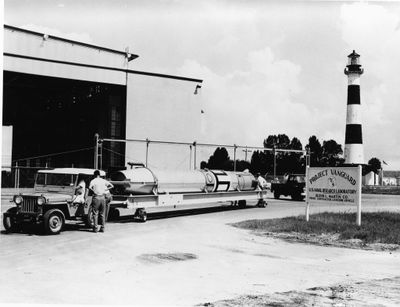 photo en noir et blanc de deux hommes debout à côté d'un camion, avec un phare en arrière-plan