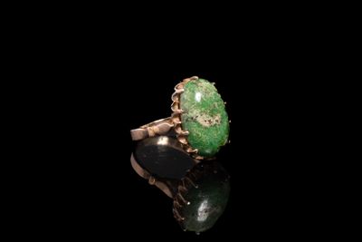 un gros plan d'une bague ornée d'une pierre verte sur un fond noir