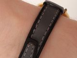 a person wearing a black leather bracelet with a gold clasp