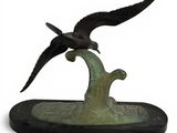 statue of a bird flying over a tree branch on a white background