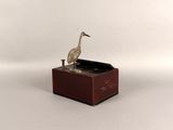 statue of a bird sitting on top of a wooden box on a white surface