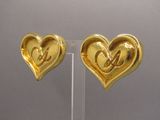 two gold heart shaped earrings with initials on them on a clear stand