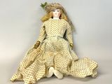 poupée assise par terre, vêtue d'une robe blanche et d'un chapeau