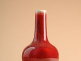 un vase rouge posé sur une table, sur fond beige