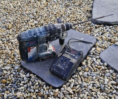 a corded drill sitting on the ground next to some rocks