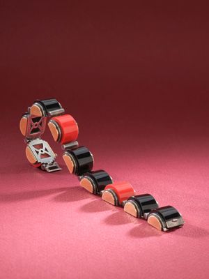 a close up of a red and black roller chain on a pink surface