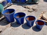three blue buckets sitting on the ground next to a pile of barrels