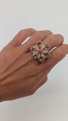 la main tient une bague en forme de fleur rose et verte
