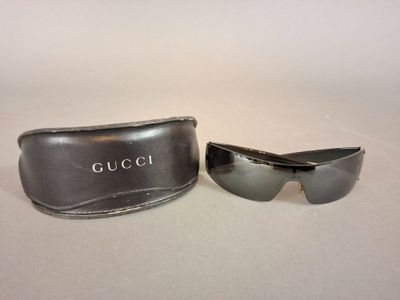 une paire de lunettes de soleil Gucci et son étui posés sur une surface blanche