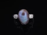 an oval pearl and diamond ring on a black surface