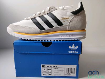 une paire de baskets Adidas blanches et noires posée sur une boîte bleue