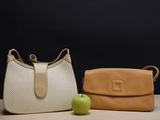 beige and white purses with apple on table against black background