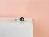 a close up of a black diamond flower ring on a white marble block