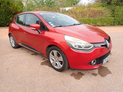 La voiture rouge est garée sur le parking, à côté des buissons.