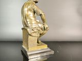 bronze statue of a man sitting on a pedestal with his hands on his knees