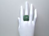 une main blanche sur laquelle est posée une bague verte