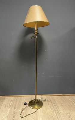 un lampadaire en laiton avec un abat-jour beige posé sur un parquet